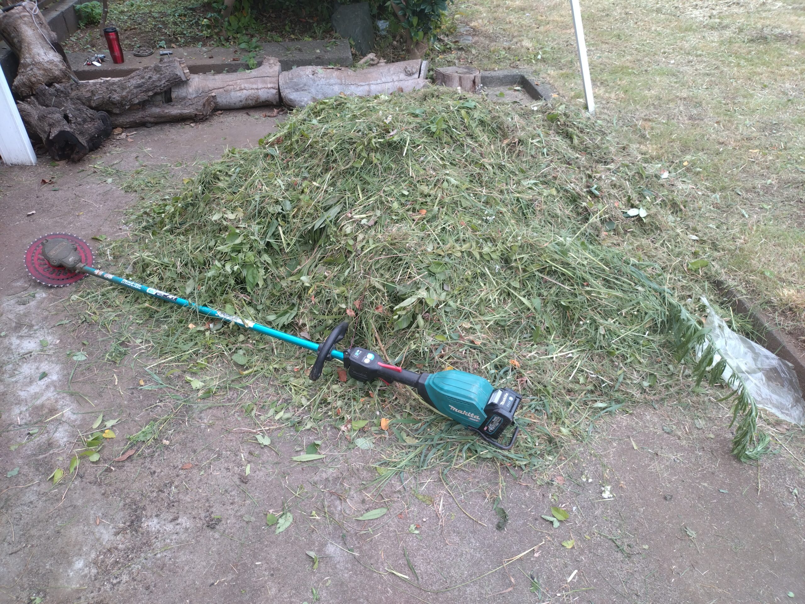 刈り取った草の山と電動草刈り機